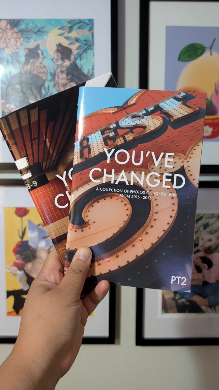 Book titled 'You've Changed PT2' held by a hand with framed artwork in the background