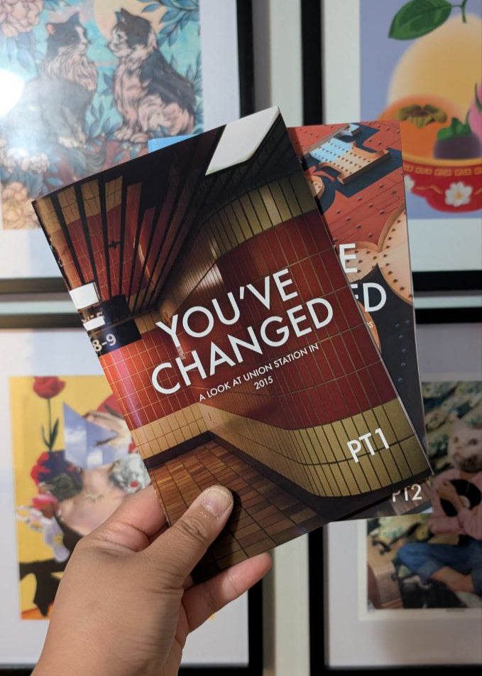 Book titled 'You've Changed' held by a hand with framed pictures in the background